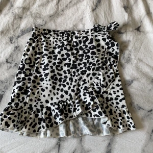 Leopard kjol - En vit volang kjol med svart leopard mönster. Säljer pågrund utav att jag inte använder. Kjolen har dragkedja så det går att justera lite på storleken. Inga defekter eller märken