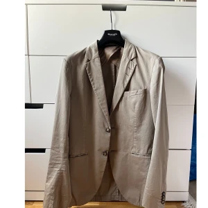 Kavaj Tiger of Sweden - Bommulskavaj från Tiger of Sweden. Väl använd, finns oklara fläckar (se sista två bilderna). Annars väldigt fin. Storlek 48.