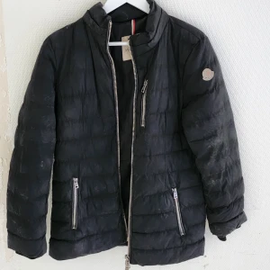 Svart pufferjacka från Moncler - Säljer en svart pufferjacka från Moncler. Jackan har en dragkedja framtill och två dragkedjefickor på sidorna. Den är långärmad och perfekt för kalla dagar. Jackan är i bra skick och väldigt bekväm att ha på sig. Passar både till vardags och lite finare tillfällen.