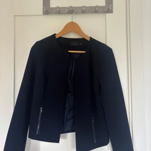 Svart kavaj från ONLY - Säljer en snygg marinblå kavaj/kappa/coat från ONLY i storlek S. Kavajen har en stilren design med dragkedjor på fickorna och en öppen framsida utan knappar. Perfekt för både vardag och fest!