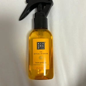 The Ritual of Mehr Home Perfume - Säljer en lyxig hemparfym från Rituals, The Ritual of Mehr. Flaskan är genomskinlig och guldfärgad med en svart spraypump. Doften är Sweet Orange & Cedar Wood, perfekt för att skapa en mysig och avslappnande atmosfär hemma. Flaskan är 50ml