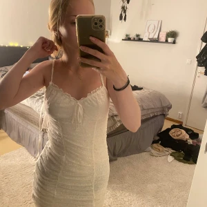 Vit klänning med spetsdetaljer - Säljer en superfin vit klänning med spetsdetaljer. Den är tight och har smala axelband. Perfekt för sommarens alla fester eller en fin middag. Klänningen är i nyskick och har en söt knytning där framme, den är väldigt bekväm att ha på sig. Passar perfekt för en somrig look! 🌸