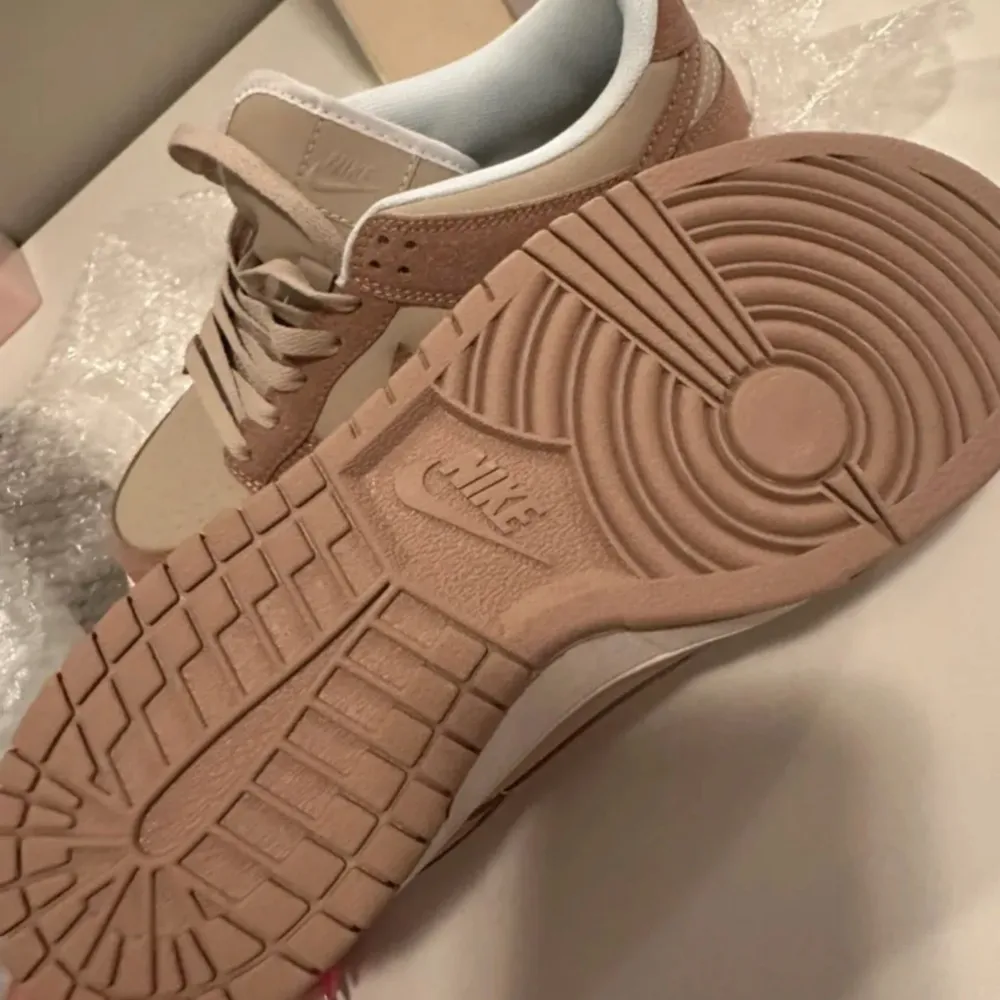 Säljer ett par snygga Nike sneakers i beige och brunt. Skorna har en klassisk design med snörning och en bekväm passform. De är tillverkade i en kombination av skinn och mocka, vilket ger dem en stilren look. Perfekta för vardagsbruk eller en avslappnad dag ute.. Skor.