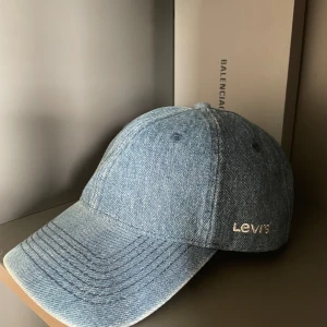 Jeanskeps från Levi's - Säljer en snygg jeanskeps från Levi's. Kepsen är i en klassisk blå jeansfärg och har Levi's logga broderad på sidan. Den har en justerbar rem baktill för perfekt passform. Perfekt för en avslappnad och cool look!