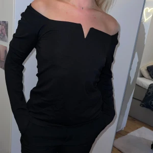Svart off-shoulder topp - Säljer en snygg svart off-shoulder topp i storlek M Toppen har långa ärmar och en liten v-ringning framtill. Perfekt för fest eller en utekväll! Toppen är i nyskick och har aldrig använts.