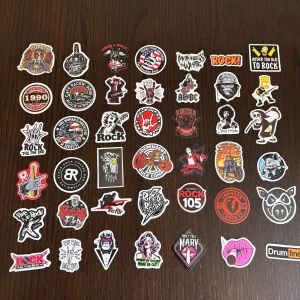 Samling av rockklistermärken - En cool samling av rockklistermärken med olika motiv och texter. Perfekt för att dekorera din gitarr, laptop, eller vägg. Klistermärkena har olika färger och stilar, inklusive bandlogotyper, rocksymboler och ikoniska bilder. De är i nyskick och redo att användas för att ge dina saker en rockig touch.