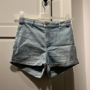 Blå jeansshorts från Divided - Ett par blå jeansshorts från Divided. Shortsen har en knapp och dragkedja framtill samt uppvikta benslut.
