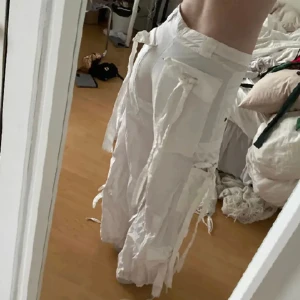 Vita 2000s lågmidjade cargo byxor - Innerben:79 cm. Midja: 38 cm. Så coola byxor med massa snören som ska knytas(dom flesta är ej knytna så snyggt eller inte alls på bild men de får man göra som man vill). Strl S. EN liten defekt på ena benet(kan skicka bild) annars felfria. Vintage<3