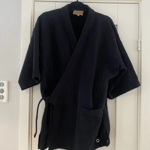 Svart kofta i kimono modell i sweatshirt material i strl M från Rue de Tokyo i nyskick  - Använd en gång i nyskick   Mått Över bröstet: ca 60 cm Längd från axeln och ner: ca 79 cm  Bomull   Kommer från ett djur och rökfritt hem.