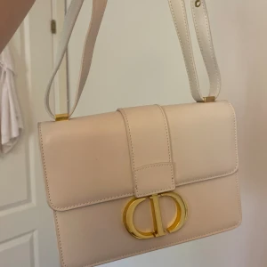 Nyskick Vit väska guld cd + bandet kan bli skärp  - Supersnygg väska Axelbandet kan bli skärp Krämvit/vit och guldig  Använd 1 gång i Nyskick förutom lite av metallen men syns knappt i verkligheten  Priset kan diskuteras lite. Färgen är som de bilderna efter den 1 bilden Fråga om mått och fler bilder.