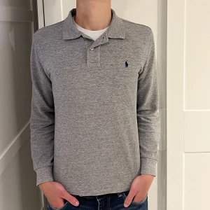 Ralph Lauren pikétröja  - Långärmad Ralp Lauren piké i färgen grå. Inga defekter på tröjan. Size S (slim fit) modellen är 177cm. Hör av dig vid funderingar!