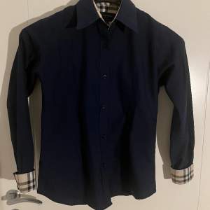 En stilig Burberry skjorta i mörkblått som säljs pga liten storlek. Använd endast ett fåtal ggr. Taggen säger S men passar även s/xs herr och M/S/XS för dam. Kan mötas upp i karlstad.