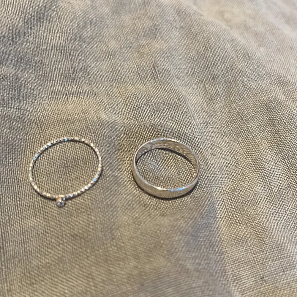 Det är två ganska tunna och små ringar i silver. Den ena har en diamant och är väldigt smal och den andra är lite större och hel silvrig.. Accessoarer.