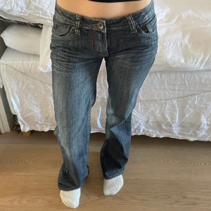 Låg midjade jeans med stenar  - Låg midjade mörk blå jeans med stenar/kristaller på fickorna  Måtten är:  Midja - 39 cm  Innerbenslängd längden - 83cm  Ben längd - 103 cm 