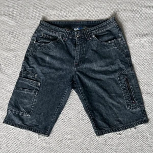 Jeansshorts från Blue Wear - Ett par mörkgrå jeansshorts från Blue Wear med flera fickor och slitna kanter. Shortsen har en avslappnad passform och är tillverkade i slitstarkt material. Köpta secondhand. Skriv för fler bilder eller frågor 🩶💙