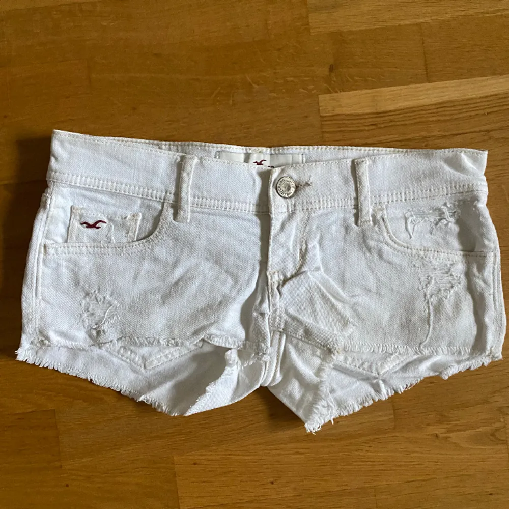 Lågmidjade vita vintage shorts från Hollister som inte säljs längre. Storlek w24, passar som xs. Midjemått: 39 cm. Lite ”slitna detaljer”, mönster på fickorna och brun Hollister detalj. Inga fläckar eller hål. Nypris 500, säljer för 250.. Shorts.