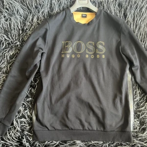 Hugo Boss Tröja  - Tröjan har använts några gånger. Köptes för 1500kr, men kan sälja den för 800kr. Färgen är svart och med guld text. Storleken är XL men den kan passa L också. 