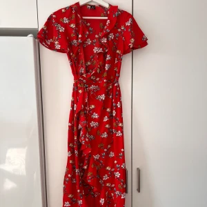 Sommarklänning  - Blommig sommarklänning i omlottmodell med volanger och kort ärm. 