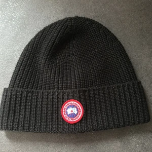 Canada Goose mössa  - Säljer en svart canada goose mössa, fick den i julklapp och tyckte inte den passade tillslut. Knappt använd har max använt den 2 gånger.