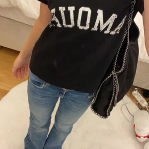 Stella McCartney liknande väska - En elegant svart axelväska med glittrig/skimrig yta och kedjedetaljer. Väskan har en modern design och är perfekt för både vardag och skolan.