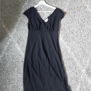 Svart klänning från Laura Clement - En svart klänning från Laura Clement med korta ärmar och v-ringad hals. Klänningen har en omlott-design och är medellång. Mycket bra skick och säljer då den är för stor för mig, men skulle uppskatta att den är storlek M.