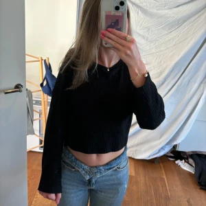 Svart stickad tröja - En svart stickad tröja med långa ärmar och en croppad passform. Tröjan har en enkel design och är bekväm att bära.