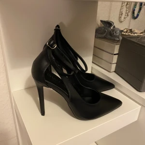 Klackar  - Svarta klackar i läderimitation. Spänne runt ankeln. Storlek 38.