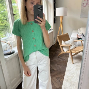 Grön ribbad topp med knappar - En grön ribbad topp med korta ärmar och knappar framtill. Toppen har en normal passform och är tillverkad i ett bekvämt material.