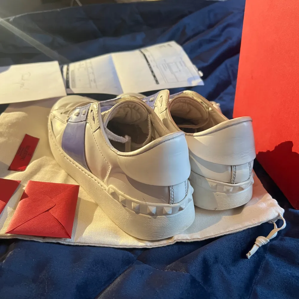 Ett par vita och lila Valentino Garavani sneakers i skinn. Skorna har snörning och en bred lila/blå rem över mitten. De kommer med originalförpackning och tillbehör. det finns även KVITTO, köpta på miinto. Skor.