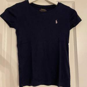 Polo Ralph Lauren T-shirt, köpt på kidsbrandstore storlek 140. Marin blå med ljus rosa märke. Lite urtvättad men inget man lägger märke till. 