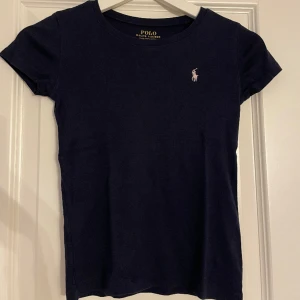 Polo Ralph Lauren T-shirt - Polo Ralph Lauren T-shirt, köpt på kidsbrandstore storlek 140. Marin blå med ljus rosa märke. Lite urtvättad men inget man lägger märke till. 