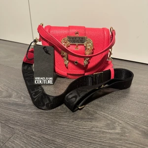 Versace handväska - Helt onanvänd Versace handväska, lappar var. Skulle säga att färgen är ceriserosa.