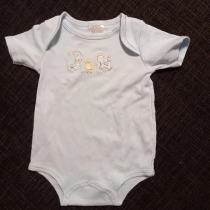 Ljusblå kortärmad body strl. 3 mån - Ljusblå kortärmad body med djur i storlek 3 månader. I fint begagnat skick, inga hål eller fläckar. Unisex.  Tvättad i parfymfritt tvättmedel och utan sköljmedel. 