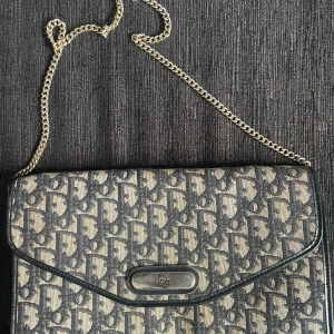 Dior väska  - Christian Dior, väska. Logomönstrad canvas med skinndetaljer. Axelremskedja i guldfärgad metall. Perfekt till balen!  Märkt "Christian Dior MADE IN FRANCE". 28 x 18 x 4 cm. Köpt på tradera  Helhetsintrycket är gott. Smärre slitage. Tryckknapp funge