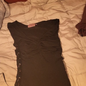 Klänning - Svart ärmlös klänning med lace up på båda sidorna och super smikrande urringing med räfflor????  Eller vad det heter??