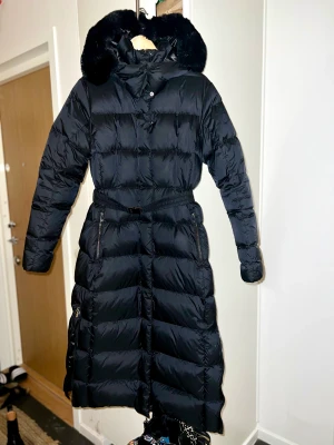 Áhkká dunkappa Gold long coat shiny  - Dunkappa i nyskick med bälte. Kan bäras utan. Svart. Lång. Varm. Avtagbar luva med svart päls. 