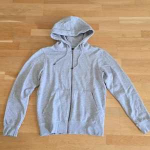 Ljusgrå hoodie från Jack & Jones XS - Säljer en ljusgrå hoodie från Jack & Jones i storlek XS. Tröjan har huva med snörning, hel dragkedja framtill och två fickor. Tillverkad i mjuk bomullsmix, perfekt för chill dagar. Enkel och stilren design som funkar till det mesta.