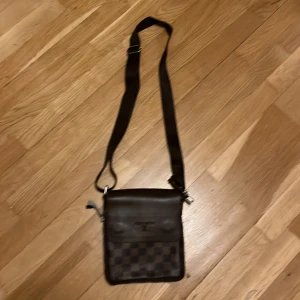 Brun axelremsväska - Brun väska med fyra fack och dragkedja som möjliggör att väskan blir rymligare. Med magnetlås.