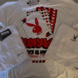 Vit Playboy t-shirt med tryck - Vit t-shirt från Playboy med stort tryck av spelkort och den klassiska kaninloggan i rött och svart. Rund halsringning och korta ärmar. Materialet är mjuk bomull som känns skönt mot huden. Perfekt för dig som gillar streetstyle och vill sticka ut med en ikonisk look.Helt nya finns i L och M