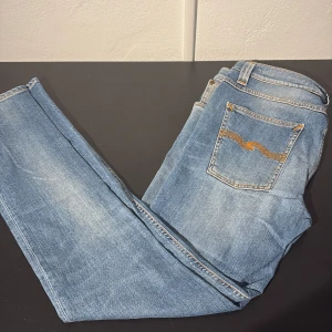 Blå jeans från Nudie Jeans - Snygga blå jeans från Nudie Jeans med klassisk femficksdesign och orangea kontrastsömmar. Jeansen har en rak passform och är tillverkade i mjukt denimtyg. Bakfickan har Nudies ikoniska broderi. Perfekta för en avslappnad och stilren look. Ny pris 1699!!