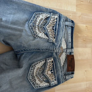 Unika bootcut jeans med bling - Jättefina ljusblå bootcut jeans med blingade detaljer och broderier på bakfickorna. ✨ Jeansen har mycket unika detaljer, coola nitar och stenar längs fickor och bälte. Jag köpte de i usa för 1200kr men de liknar miss me jeans väldigt mycket! Priset är förhandlingsbart vid en snabb affär❤️❤️❤️