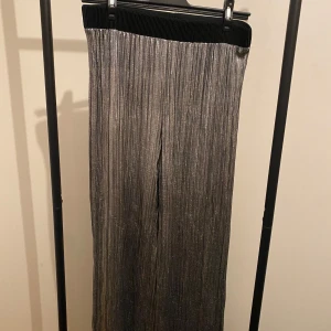 Glittriga silverbyxor från Vaschian - Säljer ett par glittriga, plisserade byxor från Vaschian i silver. Byxorna har bred resår i midjan och ett rakt, loose fit. Perfekta för dig som vill sticka ut med en cool metallic-look.