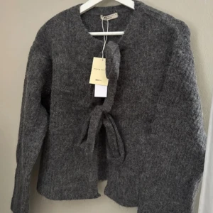 Grå stickad kofta med knyt - Superfin grå stickad kofta med två knytband som man både kan välja att ha fram eller bak. Tröjan är ifrån ginatricot.