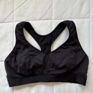 Svart sport-bh med brottarrygg - Sport-bh/topp med brottarrygg och resår nedtill. Mörkt svart, ser ljusare ut på bilderna. Tillverkad i stretchigt syntetmaterial som andas. Bra stöd. Märkt S men är mer som XS. Aldrig använd men tvättad. Skriv vid frågor 💕