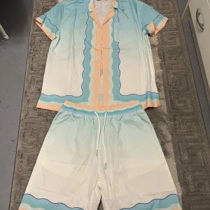 Casablanca pastell skjorta med vågmönster - Casablanca skjorta i pastellfärger med vågiga ränder i blått, beige och vitt. Kortärmad med klassisk krage och knappar framtill. Stor grafisk print på ryggen med texten 'casa' och pingisracket. Matchande shorts med dragsko ingår.