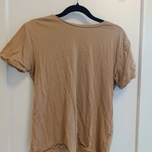 Beige basic t-shirt i bomull - Enkel beige t-shirt i mjuk bomull med rund hals och korta ärmar. Perfekt för en avslappnad stil och lätt att matcha med andra plagg. Klassisk passform och neutral färg som funkar året runt.