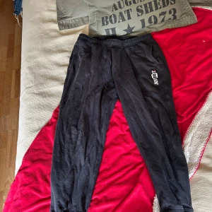 Svarta mjukisbyxor från Nike M - Svarta mjukisbyxor från Nike med elastisk midja och en liten bakficka. Byxorna har en vit och röd Just Do It-logga på ena benet och är tillverkade i mjukt bomullsmaterial. Perfekta för chill eller träning.