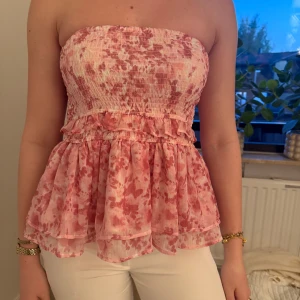 Rosa kjol med volang - Supersöt kjol i ljusrosa och vitt med volangdetaljer. Kjolen tyg är lätt och luftigt, perfekt för varma dagar. Mönstret är blommigt och ger en romantisk vibe. Passar dig som gillar feminina och trendiga plagg. Kan även användas som topp! Skriv för fler bilder eller frågor❤️