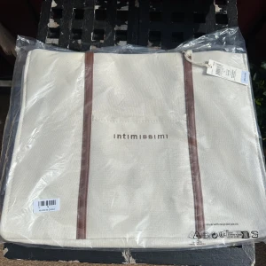 Beige weekendbag från Intimissimi💕 - Stilren beige väska från Intimissimi med bruna detaljer längs sidorna. Väskan är tillverkad i bomull och har ett minimalistiskt tryck med varumärket på framsidan. Perfekt storlek för att bära med sig allt man behöver under dagen, till stranden eller landet💕