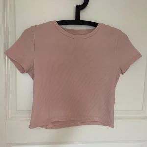 Ljusrosa ribbad croppad topp - Supersöt ljusrosa croppad topp med ribbad struktur och rund hals. Kortärmad och i mjukt, stretchigt material som sitter snyggt på kroppen. Perfekt att styla med jeans eller kjol för en chill look.